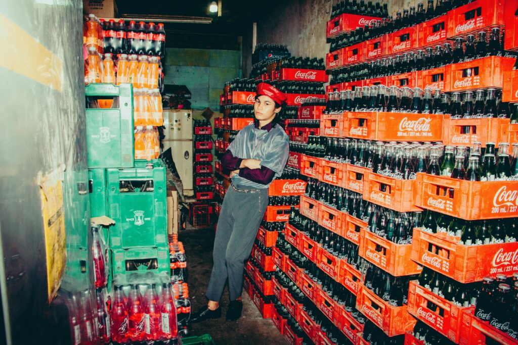 Stylish model posing among soda crates in a colorful warehouse.